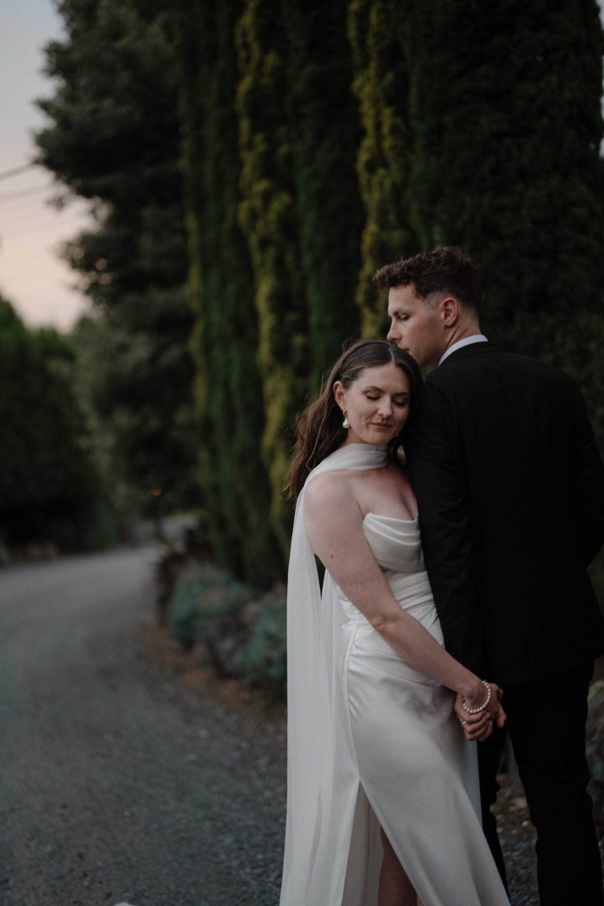 Couple standing together beside cypress trees at dusk