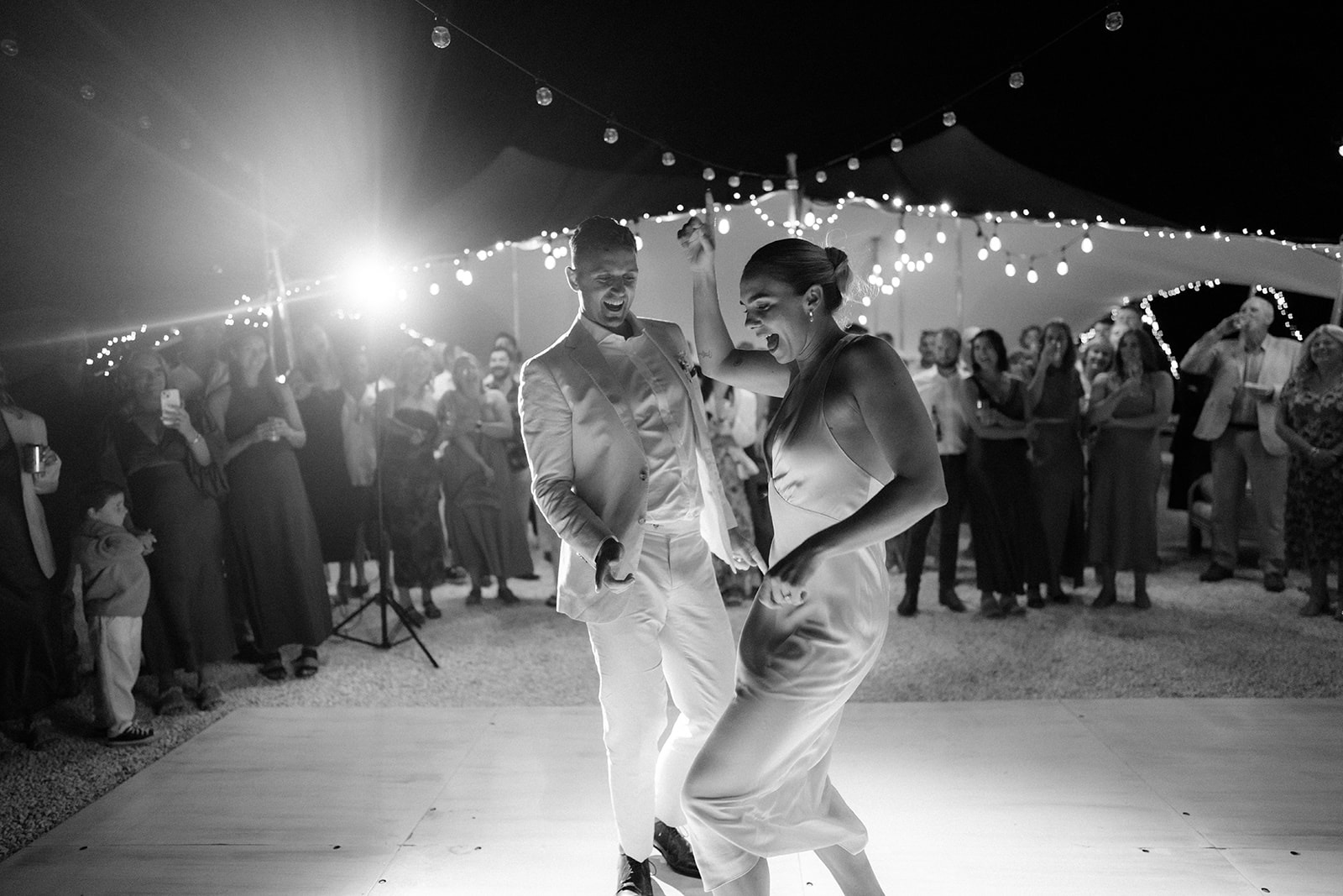 Couple dancing under festoon lights as guests cheer
